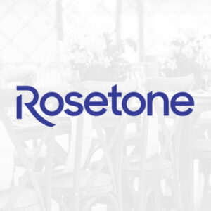 A logo with the text "Rosetone" in blue font is centered on a semi-transparent overlay. In the background, there are blurred images of event furniture, wooden chairs, and a table adorned with flowers and glassware, set in a dining or event setup.